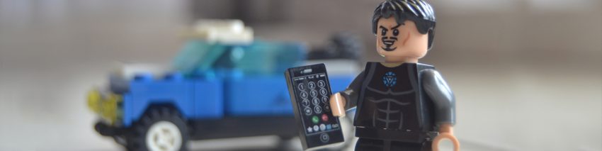 Lego minifigure holding a Lego mobile phone and standing in front of a blue Lego utility truck