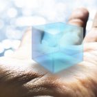Against the backdrop of a sparkling lake, an outstretched palm holds a blue, virtual cube.