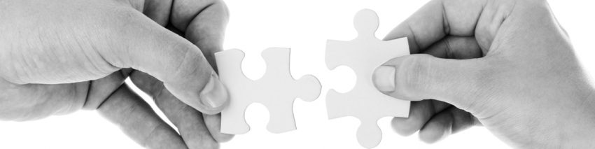 Black and white photo of two hands fitting two puzzle pieces together